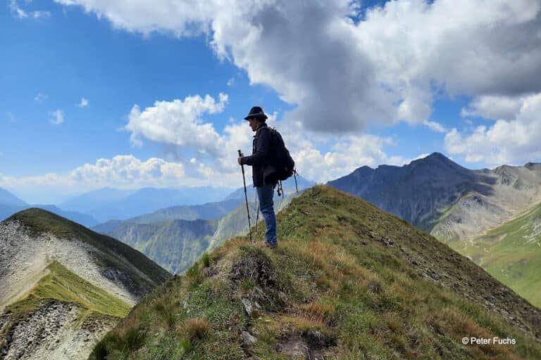 Mann auf einem Berggipfel mit Alpenpanorama